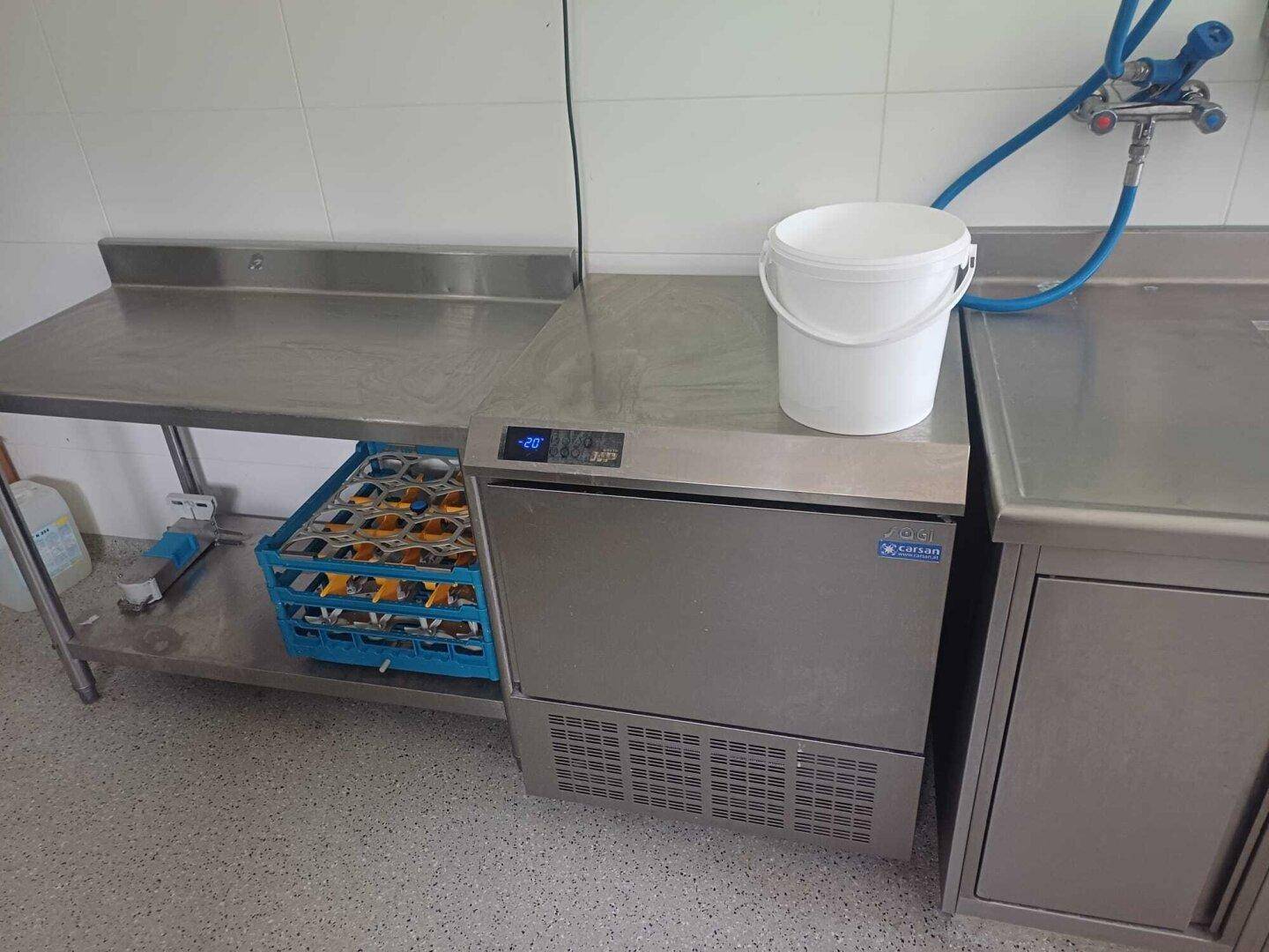 Edelstahl-Arbeitsplatte mit integriertem Eisbereiter oder Kühleinheit und einem Eimer.