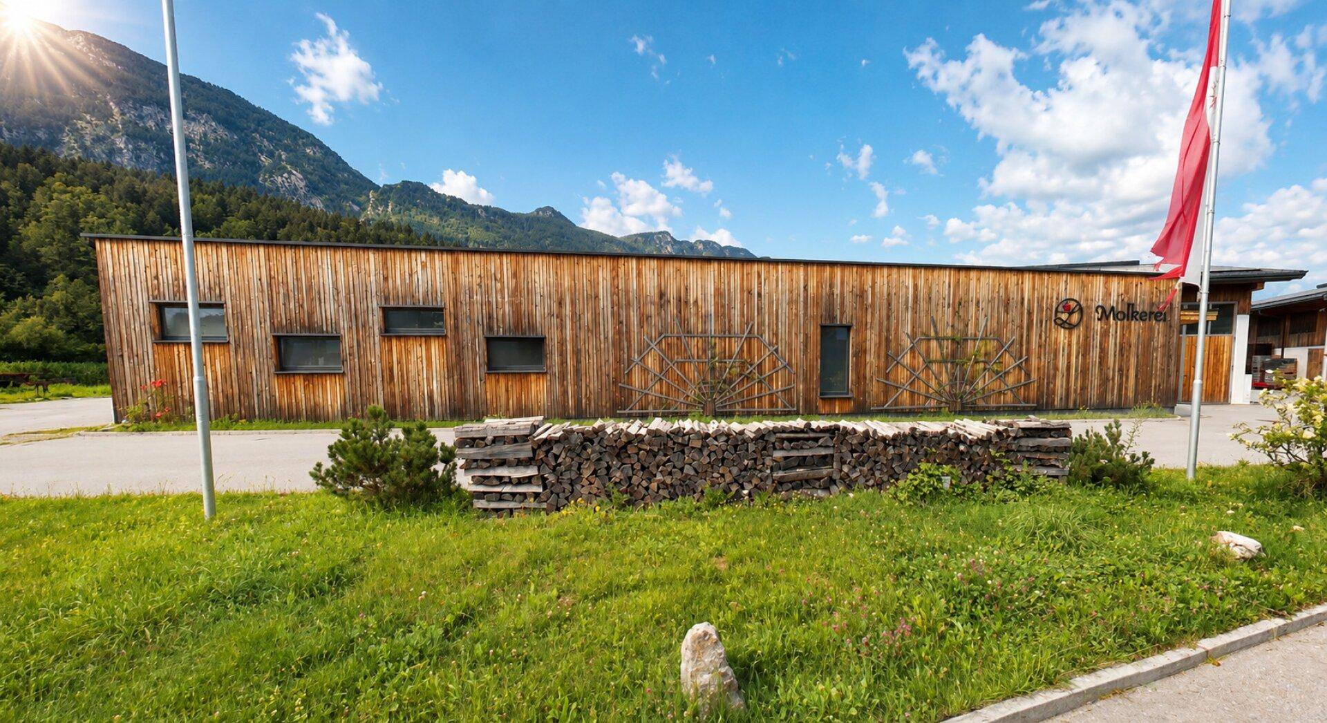 Holzverkleidetes Gebäude mit gestapeltem Brennholz und majestätischer Bergkulisse im Hintergrund.
