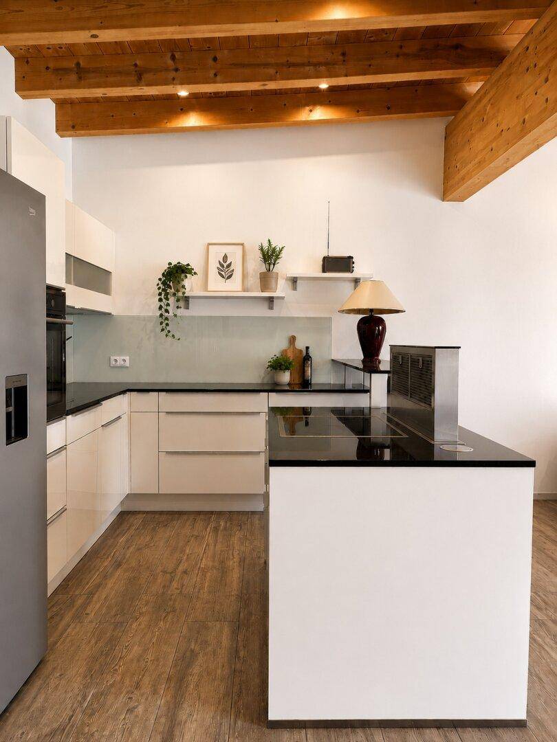 Moderne Küche mit weißen Schränken, schwarzen Arbeitsplatten, Holzboden und sichtbaren Deckenbalken.