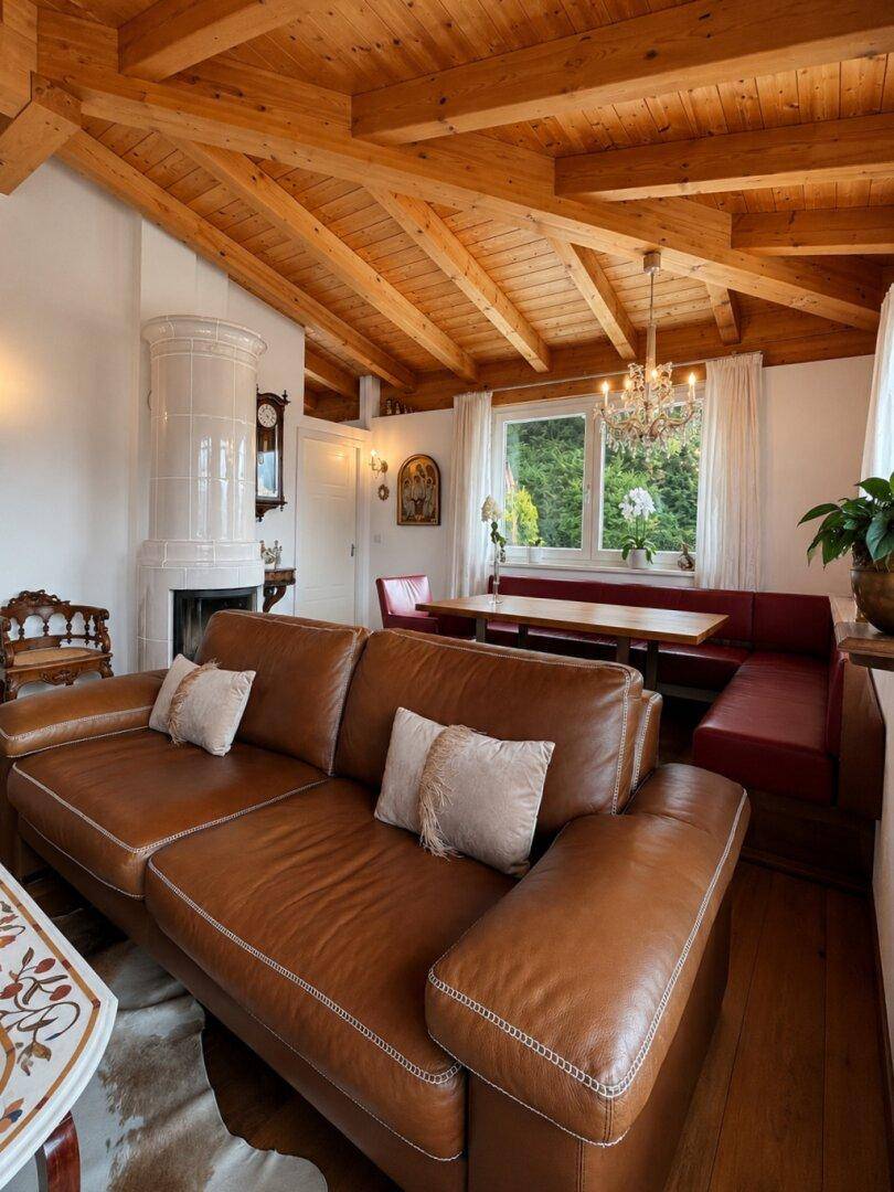 Gemütlicher Wohn-Essbereich mit Holzbalkendecke, Kachelofen und Ledersofas, ideal für gesellige Stunden.