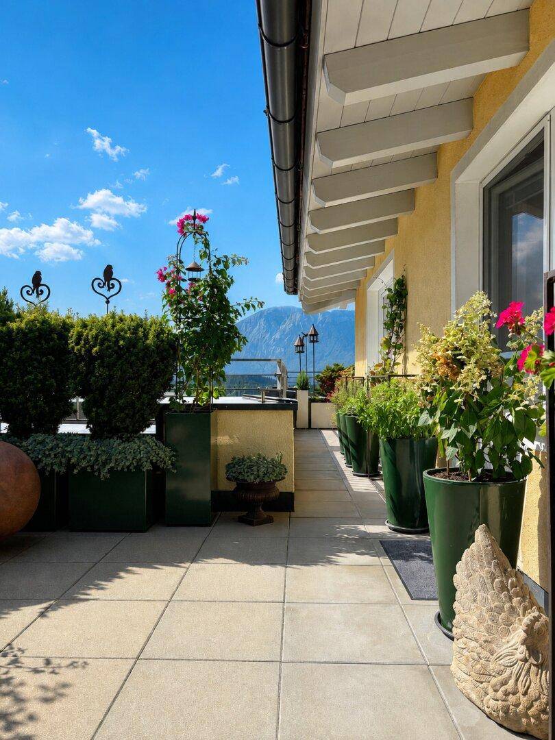 Sonnenterrasse mit Bergblick, üppiger Bepflanzung und Fliesenboden, perfekt für Outdoor-Aktivitäten.