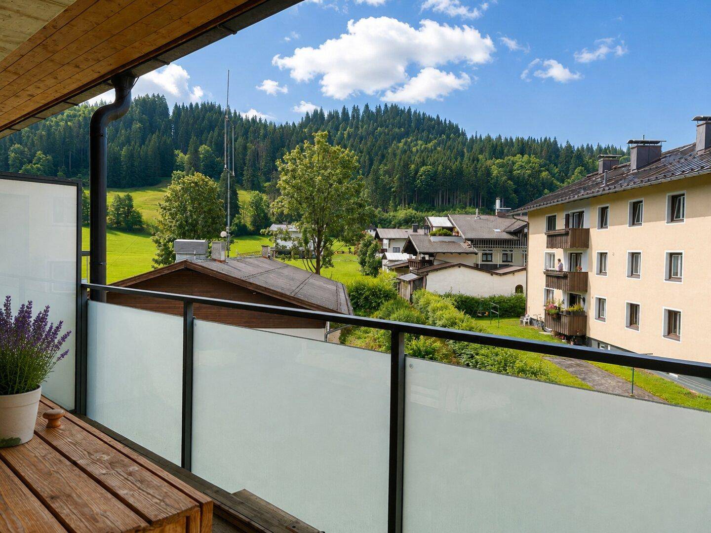 Balkon mit Holztisch und weitem Blick auf die grüne Hügellandschaft und umliegende Häuser.