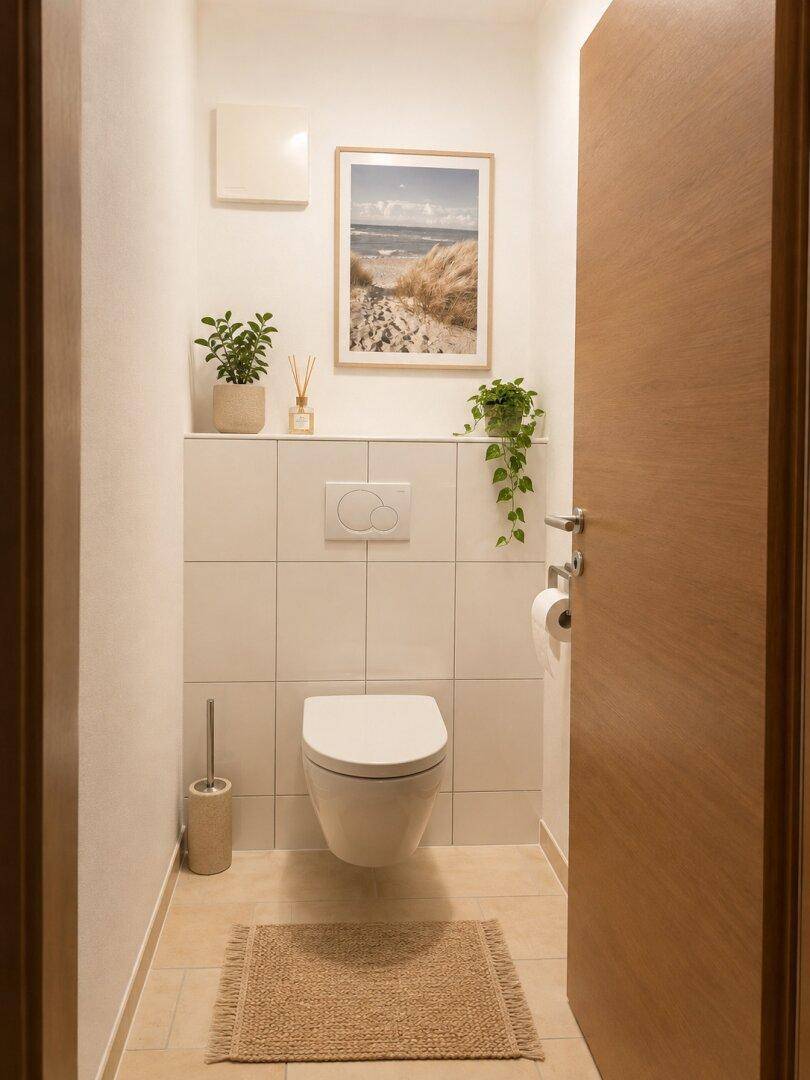 Separates Gäste-WC mit wandhängender Toilette, weißen Fliesen und einem kleinen Waschbecken.
