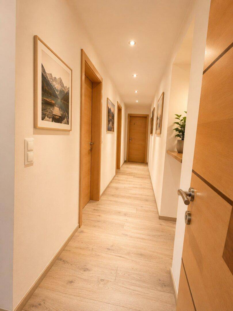 Langer Flur mit Holzboden, hellen Wänden und Bildern an der Wand.