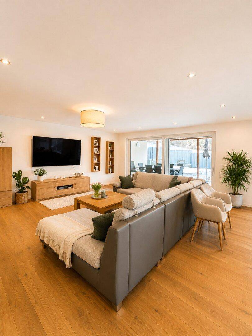 Geräumiges Wohnzimmer mit großem Sofa, Holzboden und Blick auf den Außenbereich.