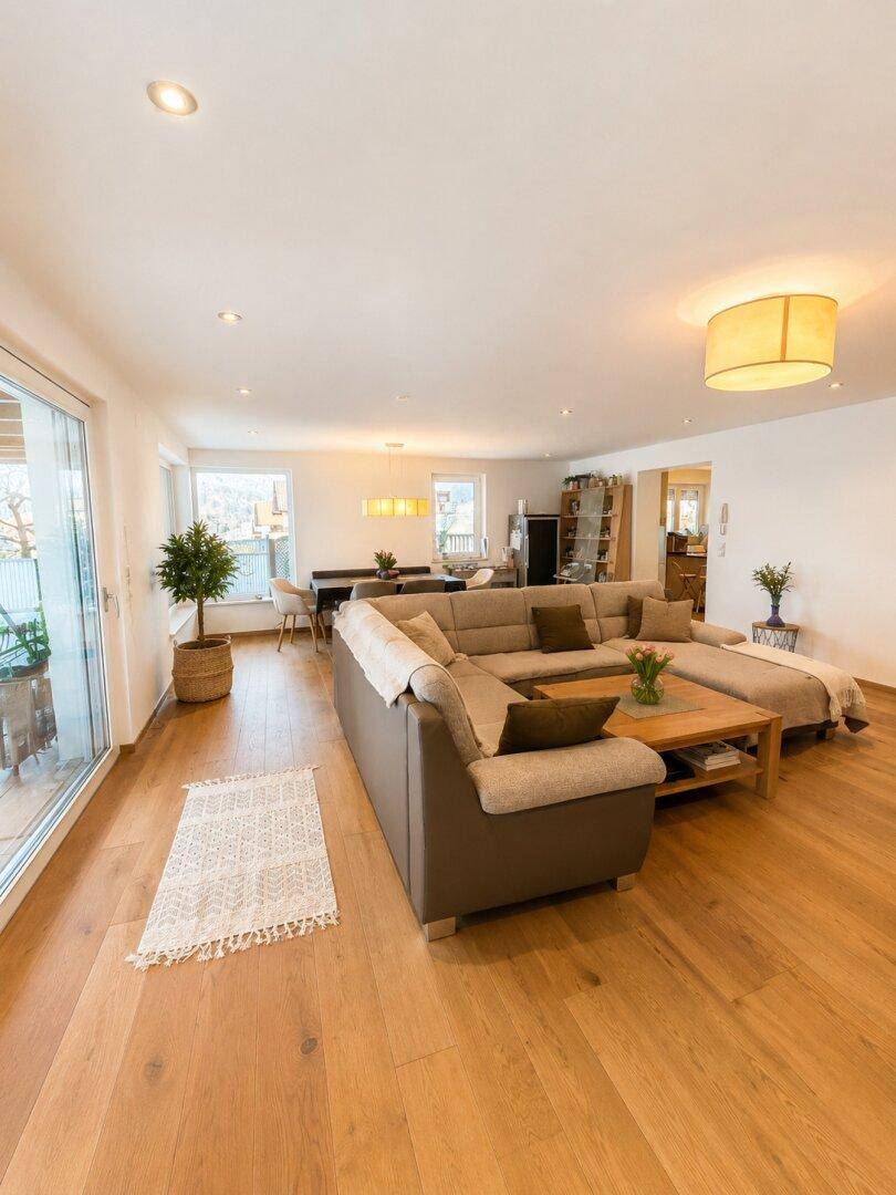 Heller offener Wohn- und Essbereich mit Holzboden und Zugang zum Balkon.