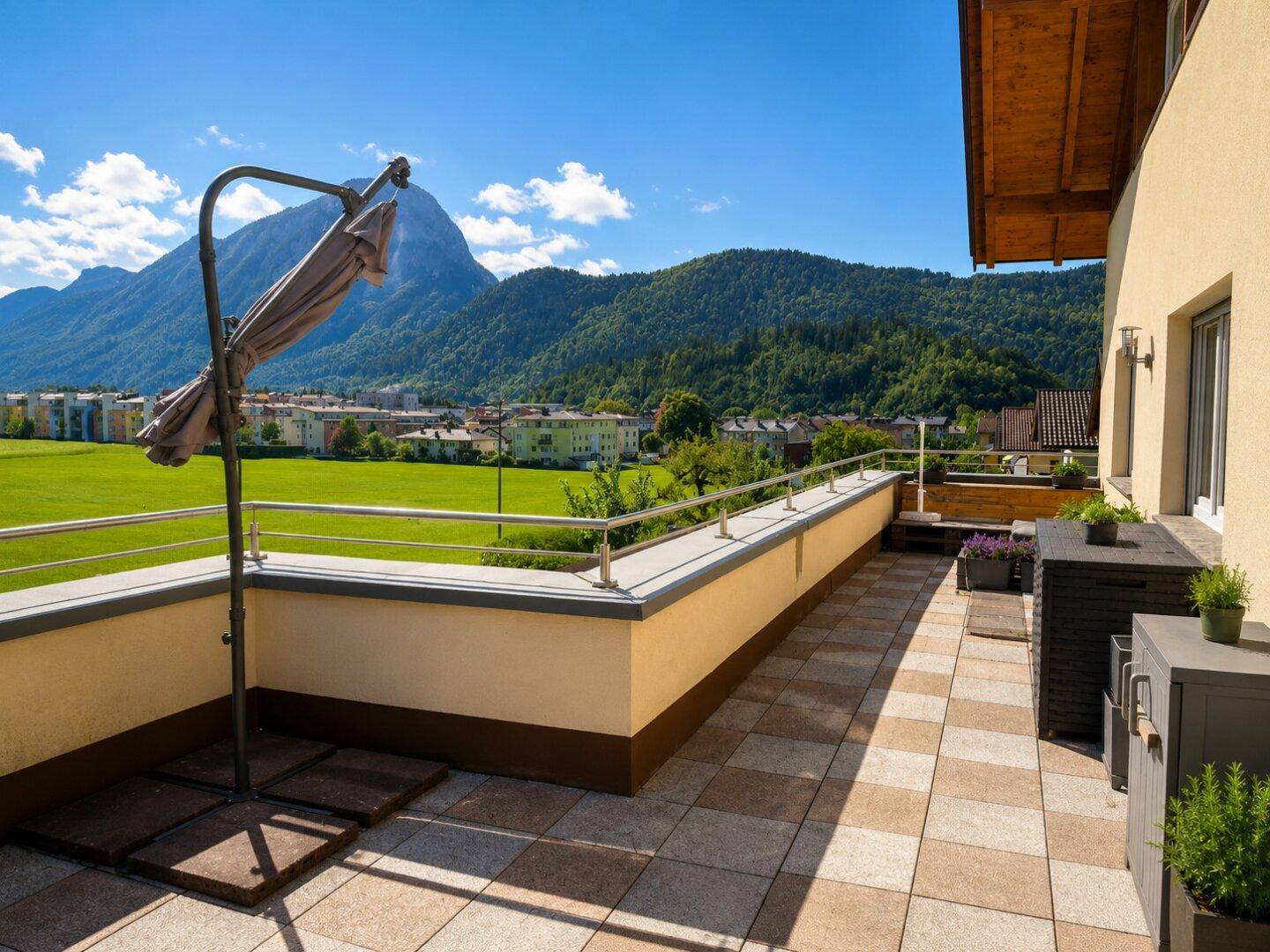 Weitläufige Terrasse mit Fliesenboden, Sonnenschirm und weitem Blick über die grüne Landschaft und Berge.