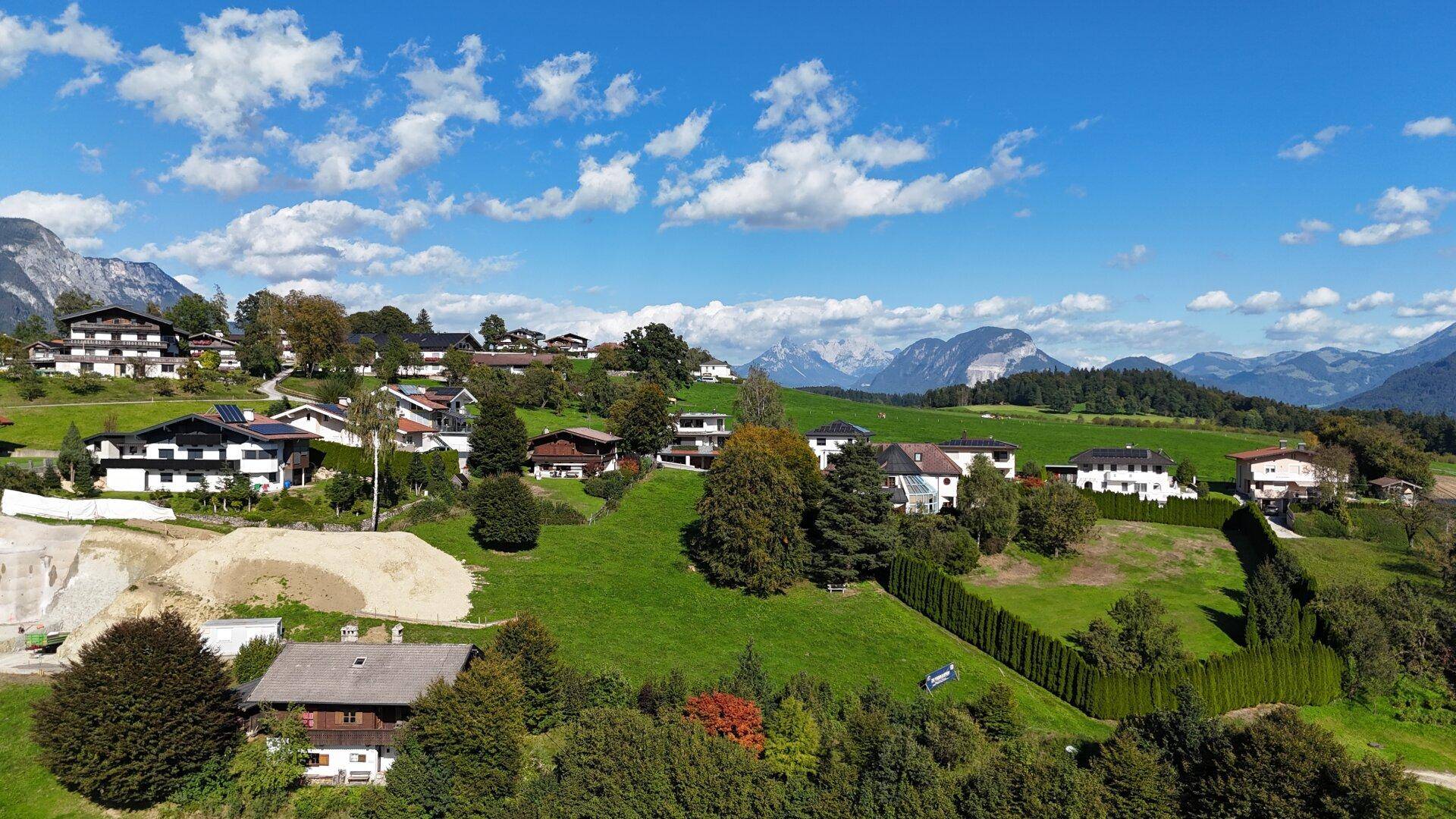 Weitläufige Ansicht einer Wohngegend in den Alpen mit grünen Wiesen und schneebedeckten Berggipfeln am Horizont.