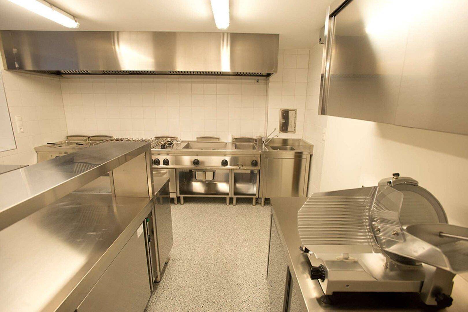 Blick in die Industrieküche mit professioneller Aufschnittmaschine und weiteren Edelstahl-Arbeitsflächen.