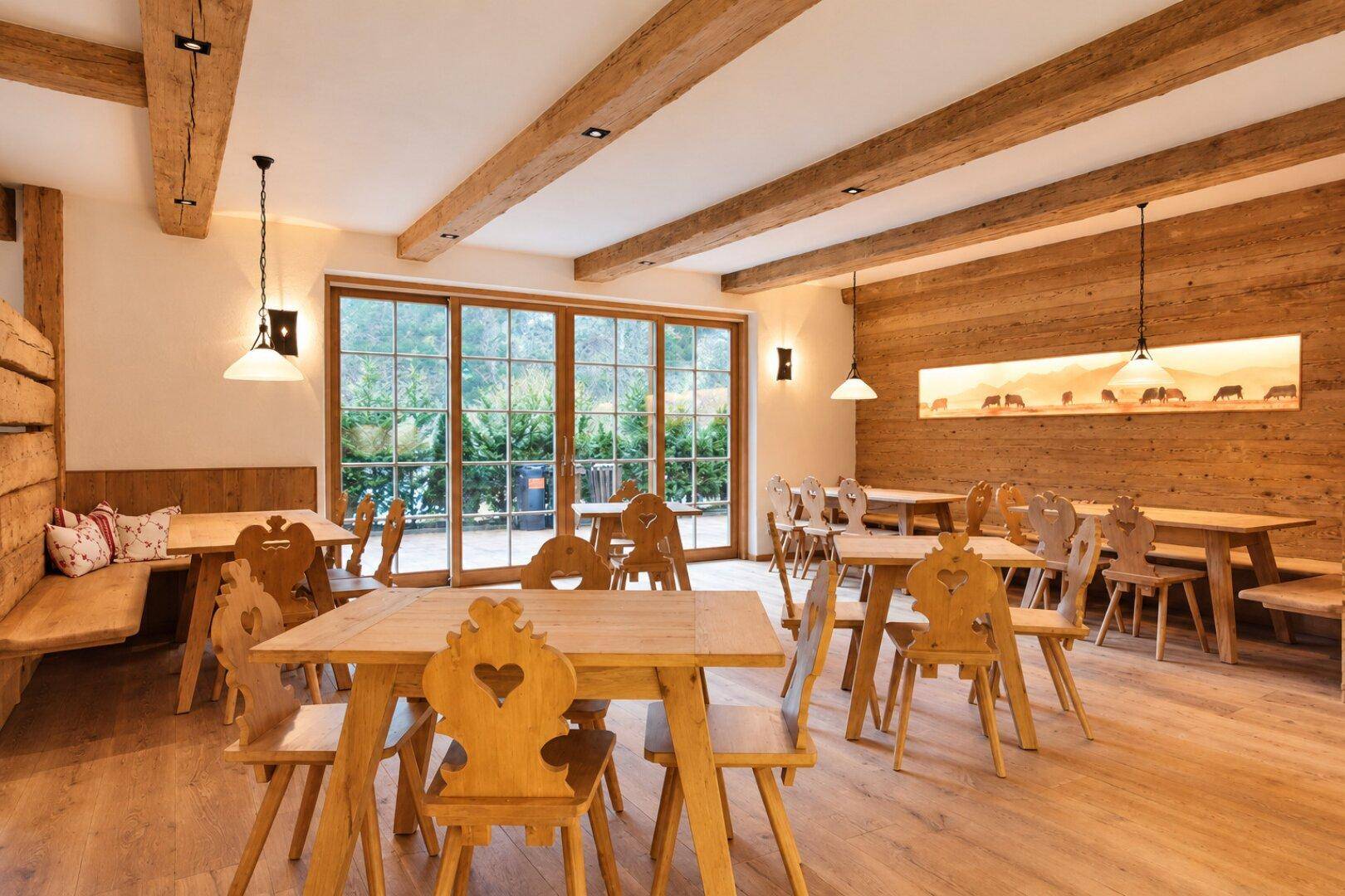 Geräumiger Speisesaal mit vielen Holztischen und Stühlen, sichtbaren Deckenbalken und viel Tageslicht.