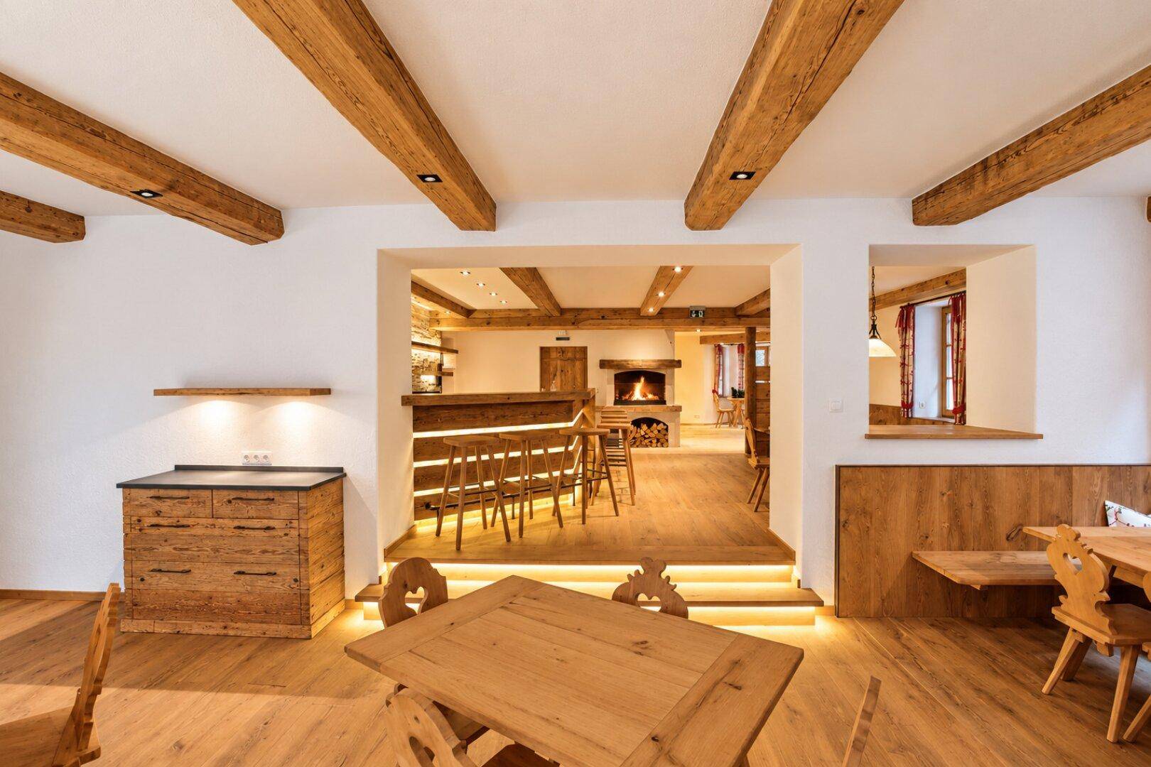 Essbereich mit Blick auf die Bar und den Kamin, verbunden durch beleuchtete Stufen und Holzelemente.