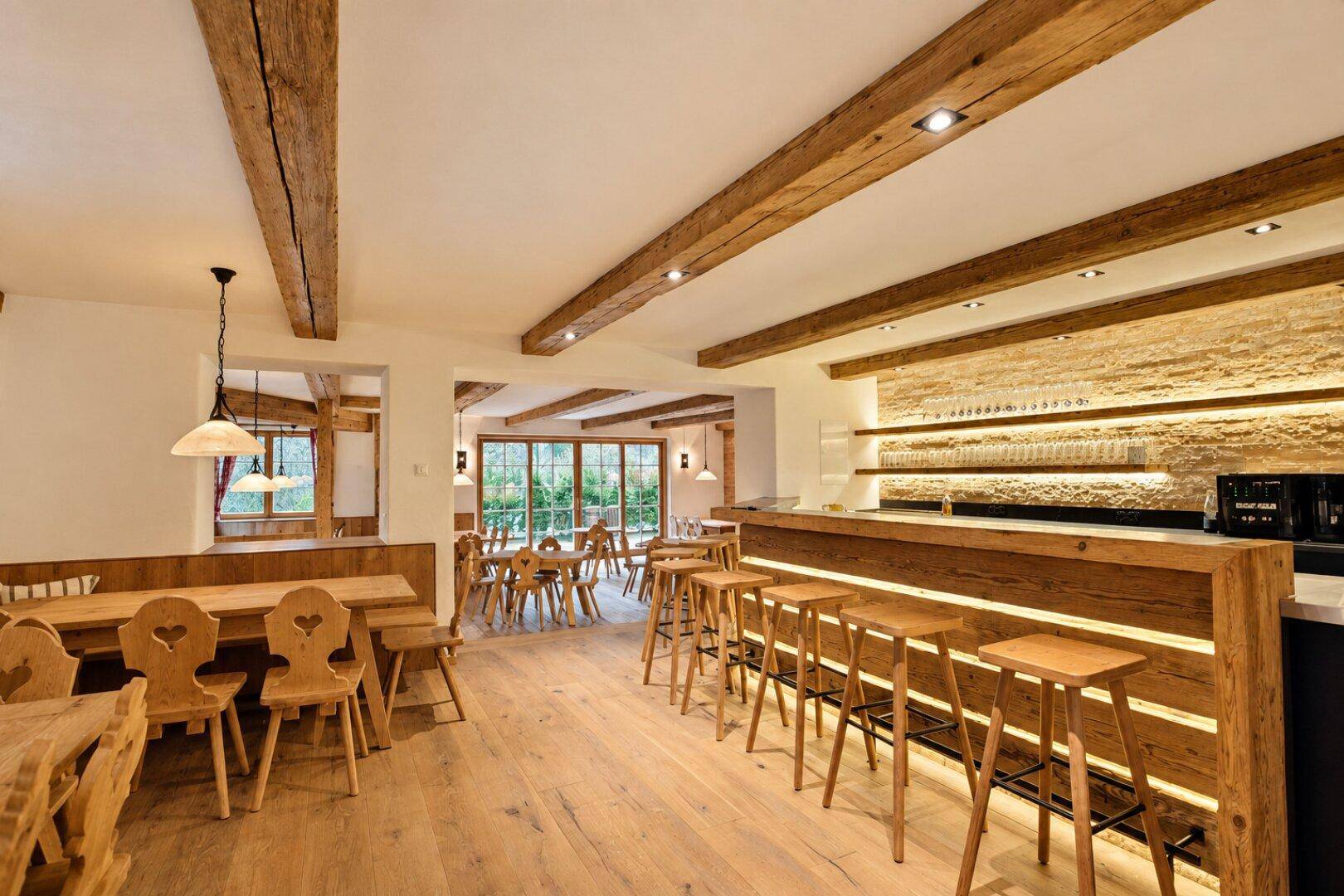 Rustikale Bar mit Holzhockern und beleuchteter Steinwand, angrenzend an einen traditionellen Speisebereich.