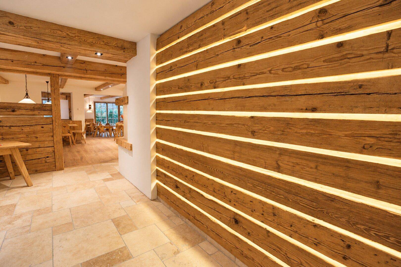 Flur mit Steinboden und einer dekorativen Wand aus beleuchteten Holzplanken, die eine warme Atmosphäre schafft.