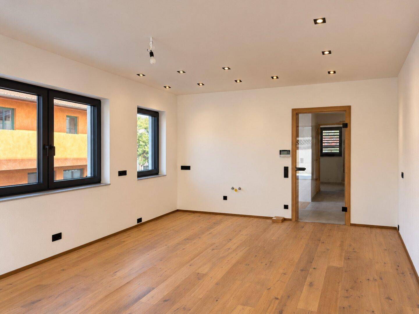 Geräumiges, helles Zimmer mit Holzboden und mehreren Fenstern, bereit zur individuellen Gestaltung.