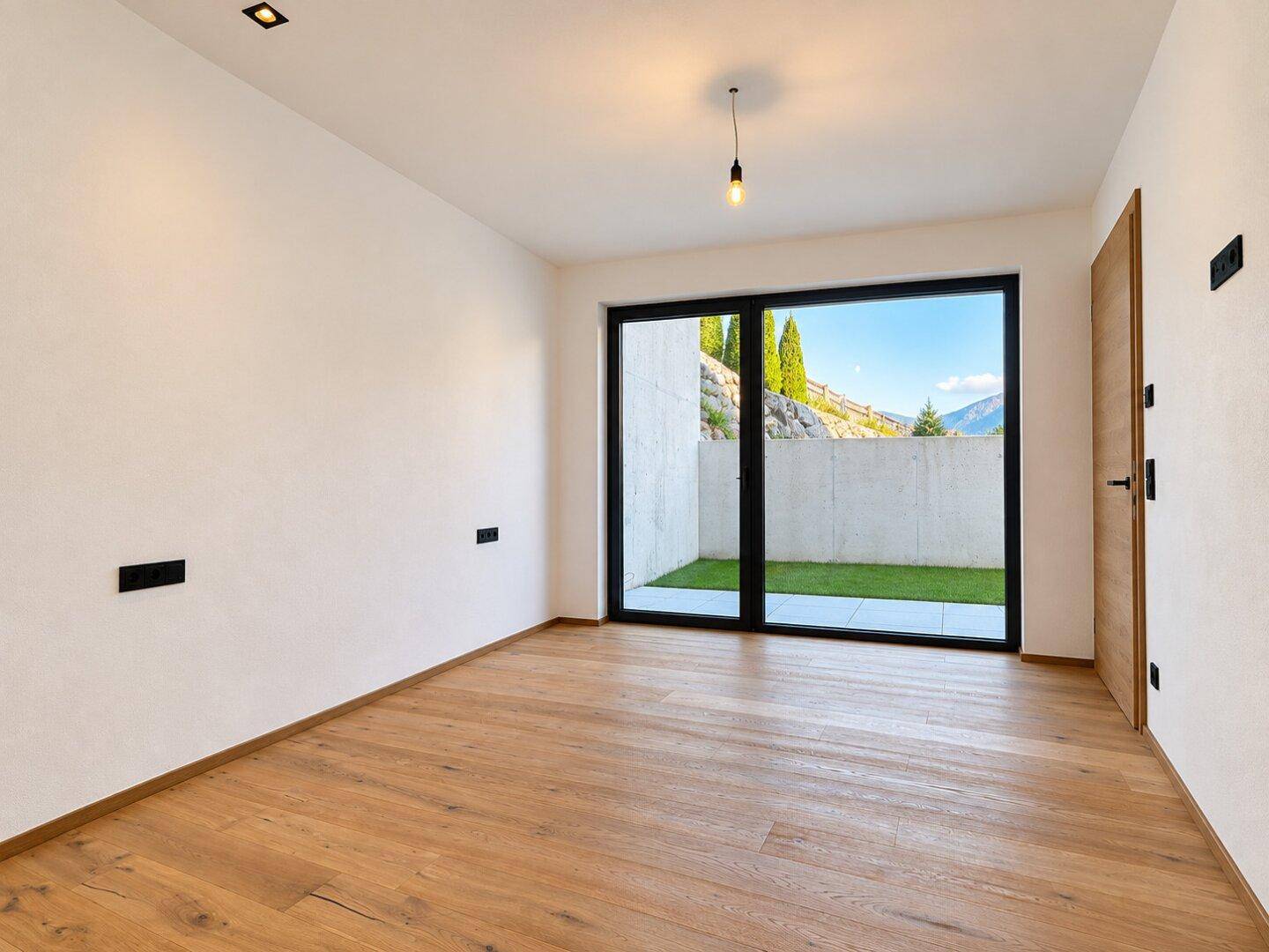 Helles Zimmer mit Holzboden und großer Glastür, die direkten Zugang zu einem kleinen Außenbereich bietet.