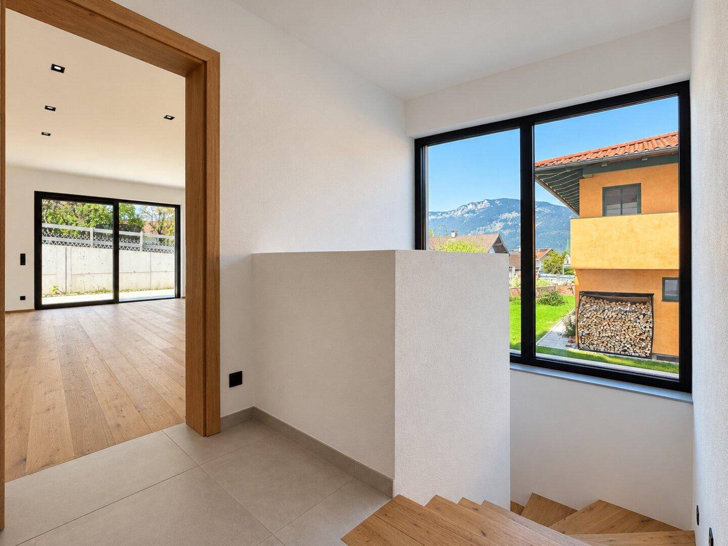 Heller Flur mit Holztreppe und Blick durch das Fenster auf die umliegende Berglandschaft.