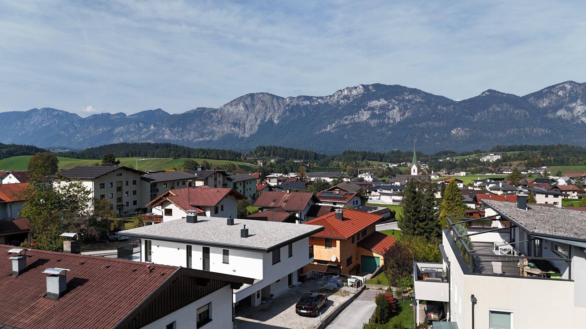 Panoramablick auf eine Wohnsiedlung mit Bergen im Hintergrund unter blauem Himmel.