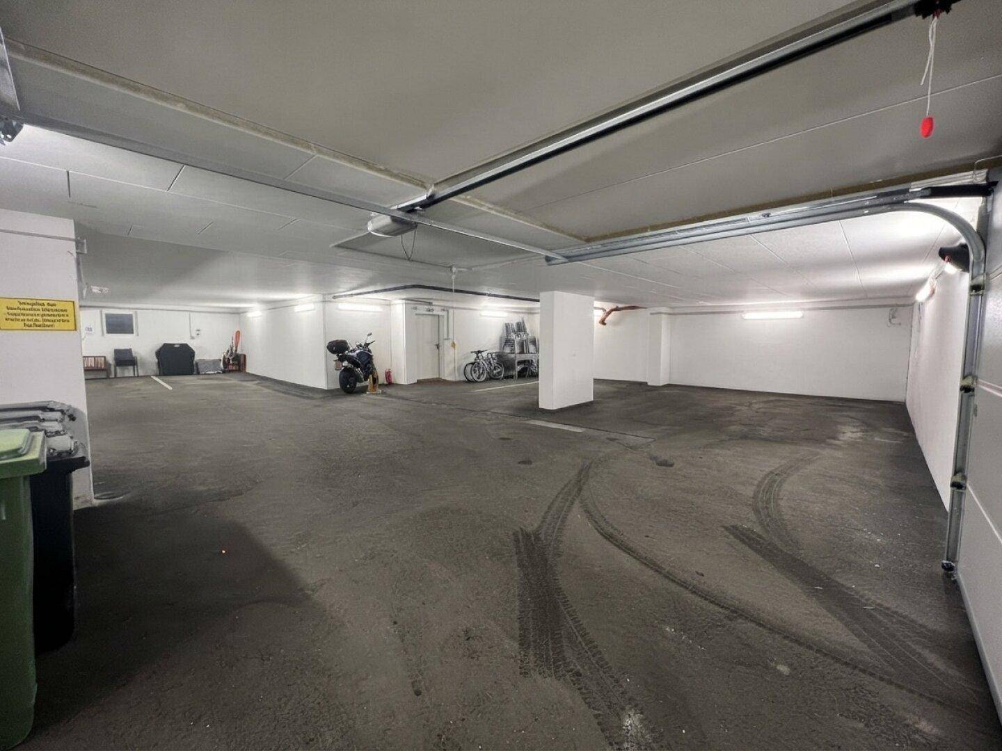Geräumige Tiefgarage mit Betonboden, weißen Wänden und ausreichend Platz für Fahrzeuge und Fahrräder.