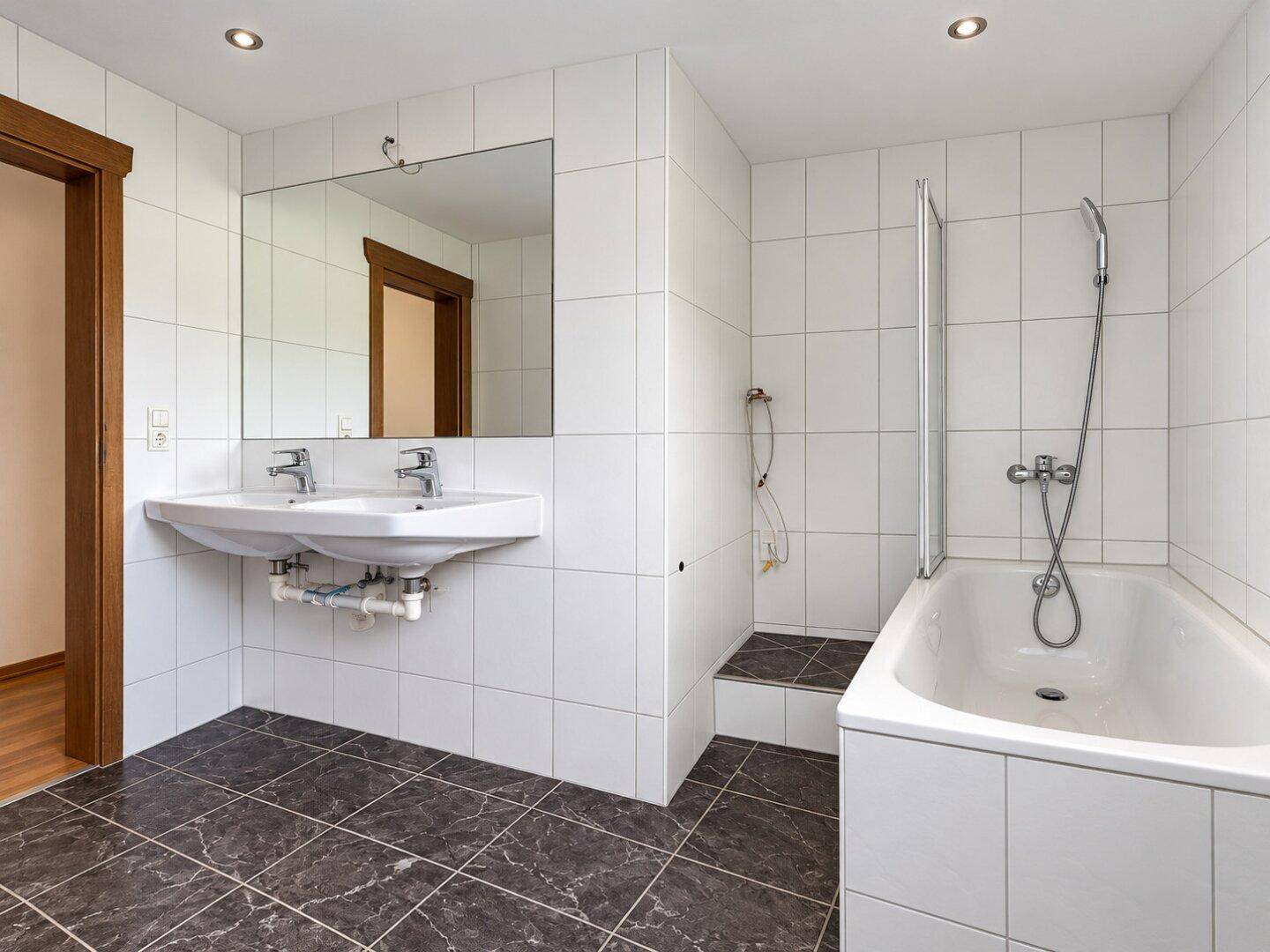 Geräumiges Badezimmer mit Doppelwaschbecken, Badewanne und Duschbereich, komplett gefliest.