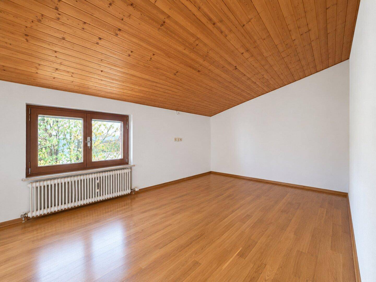 Helles Schlafzimmer mit Holzboden, Holzdecke und Fenster mit Blick ins Grüne.