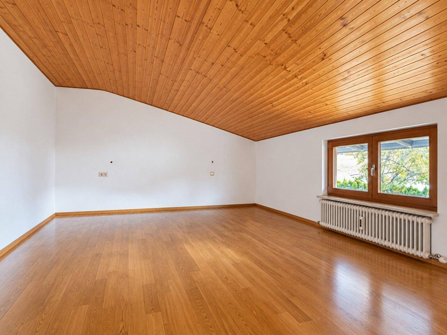 Helles Schlafzimmer mit Holzboden, Holzdecke und Fenster mit Blick ins Grüne.