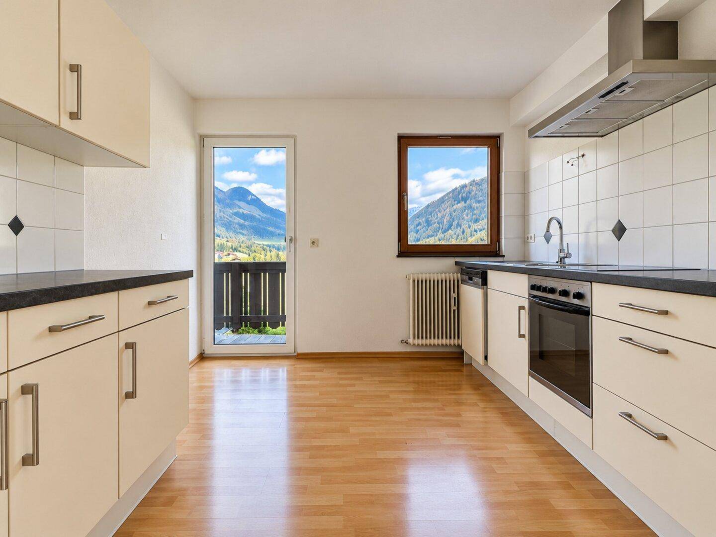 Funktionale Küche mit hellen Schränken, Holzboden und Balkonzugang mit Bergblick.