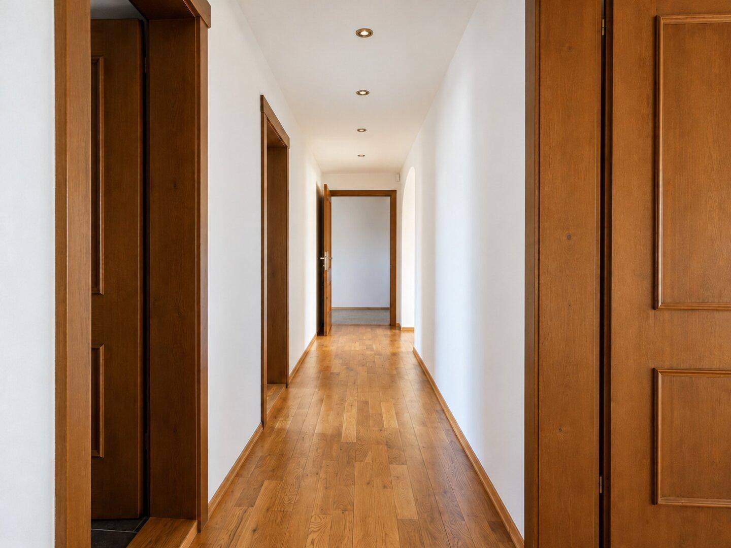 Heller Flur mit Holzboden und Holztüren, der zu verschiedenen Räumen führt.