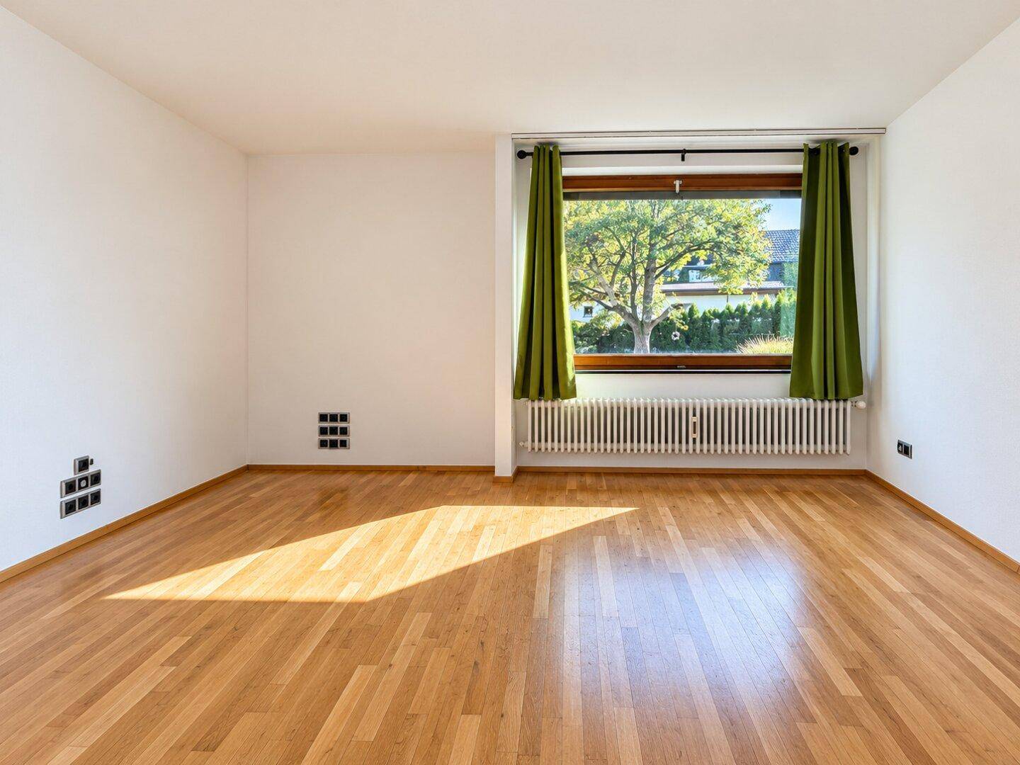 Helles Wohnzimmer mit Holzboden und großem Fenster mit Blick ins Grüne.