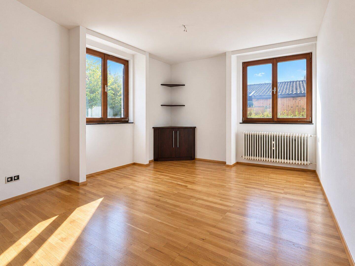 Geräumiges Zimmer mit Holzboden und zwei Fenstern, die viel Tageslicht hereinlassen.