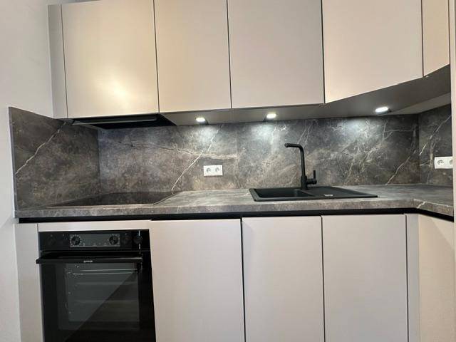 Moderne Einbauküche mit dunkler Arbeitsplatte, Induktionskochfeld und integriertem Backofen.