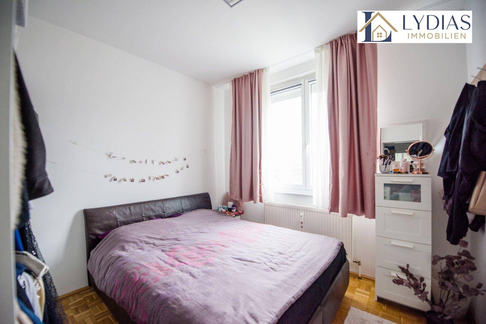 Gemütliches Schlafzimmer mit Doppelbett, hellem Fenster und rosa Vorhängen.