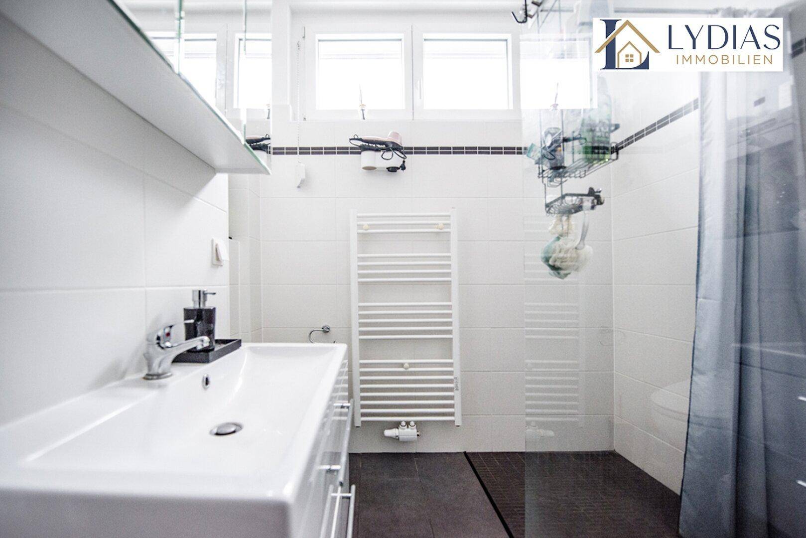Modernes Badezimmer mit Dusche, Waschbecken, beheiztem Handtuchhalter und Fenster.