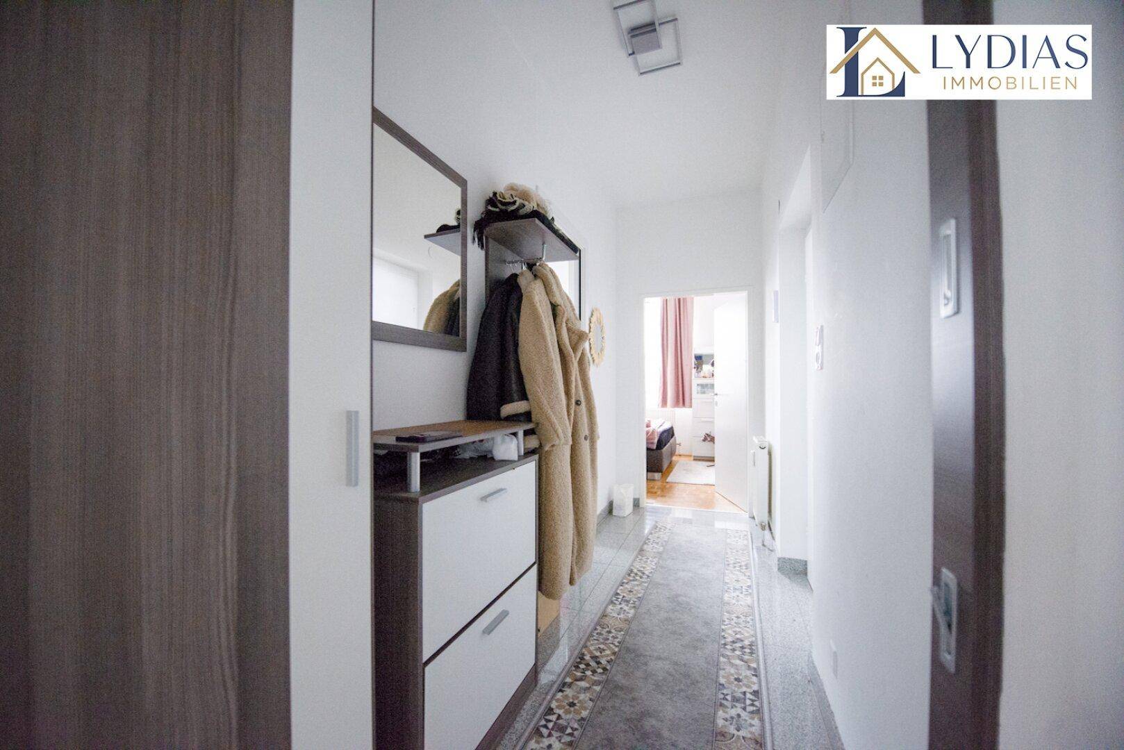 Heller Flur mit Garderobe, Spiegel und Schuhschrank, der zum Wohnbereich führt.