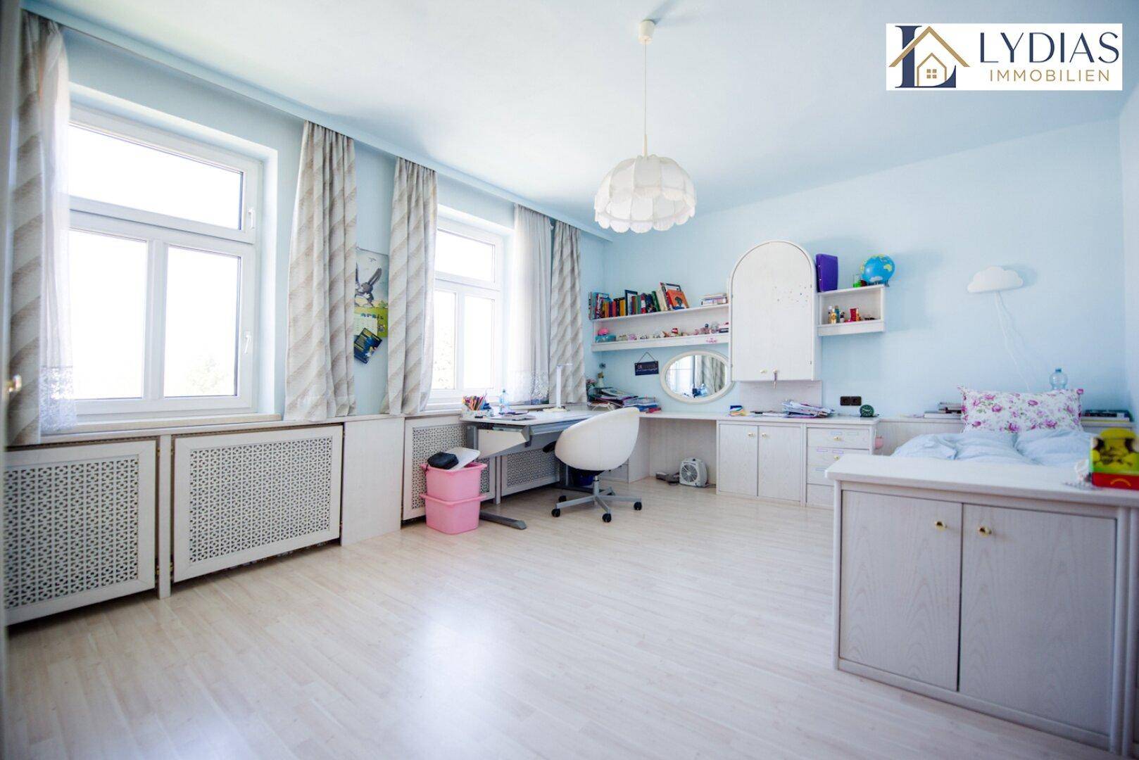 Helles Kinderzimmer mit blauen Wänden, Schreibtisch und Fenster mit viel Tageslicht.