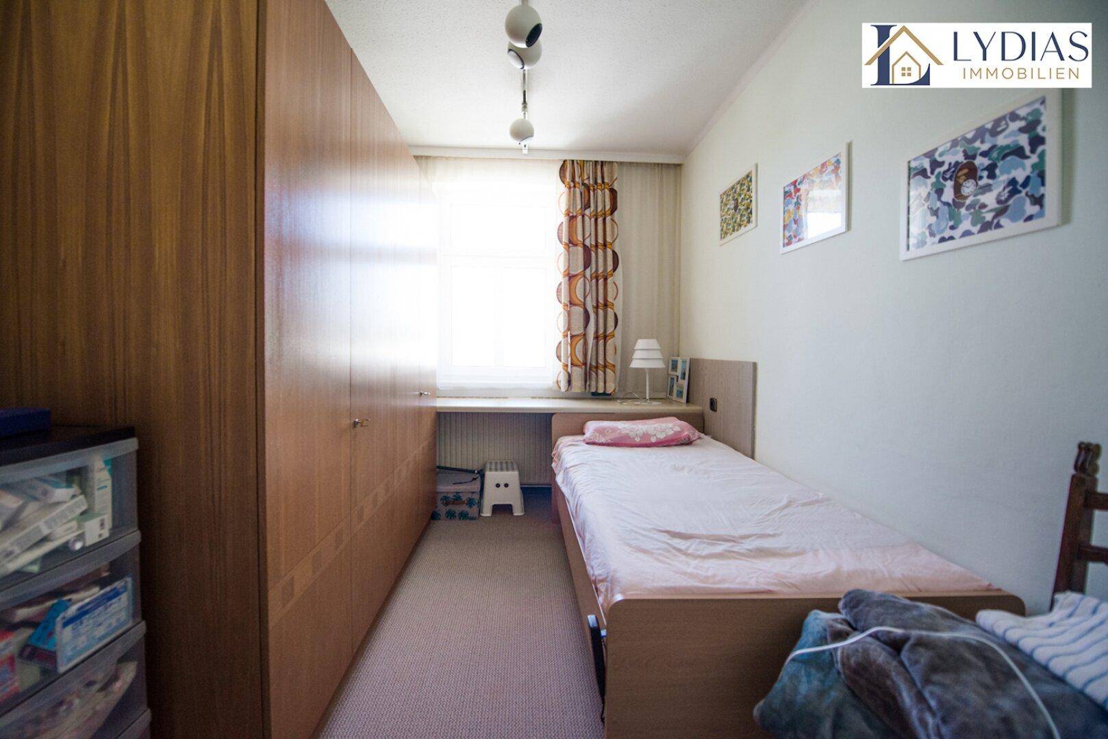 Schmales Schlafzimmer mit Einzelbett, Einbauschränken und Fenster für Tageslicht.