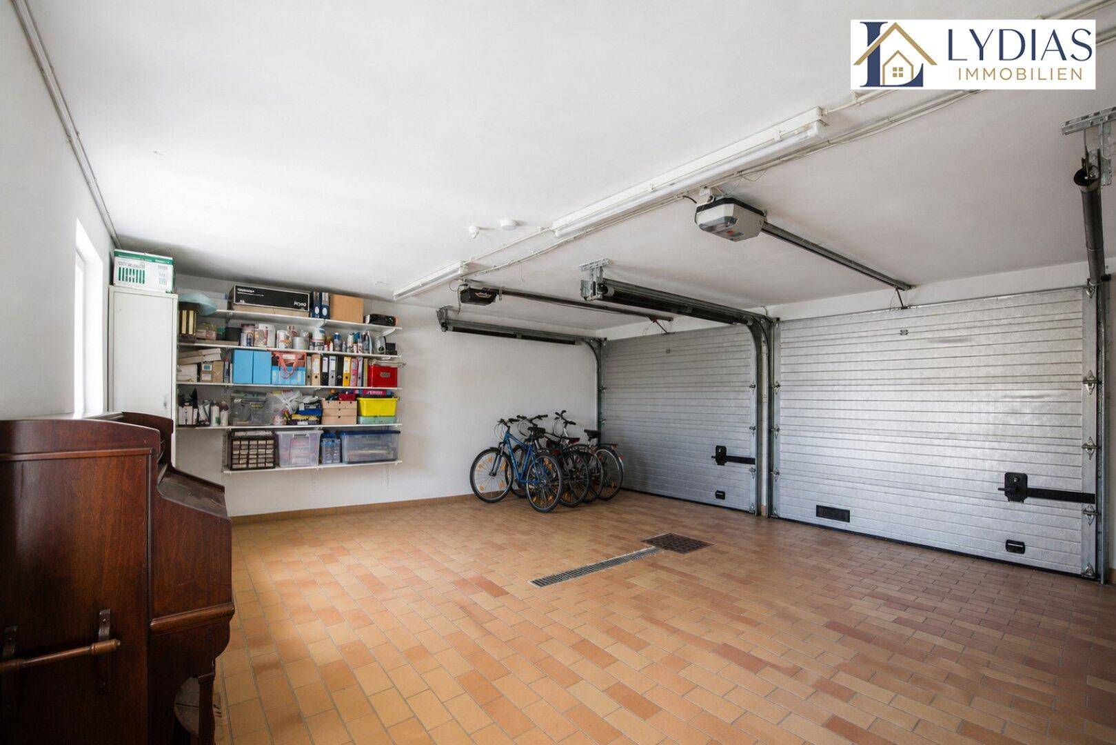 Geräumige Garage mit zwei Rolltoren, Fliesenboden und viel Stauraum für Fahrräder und mehr.