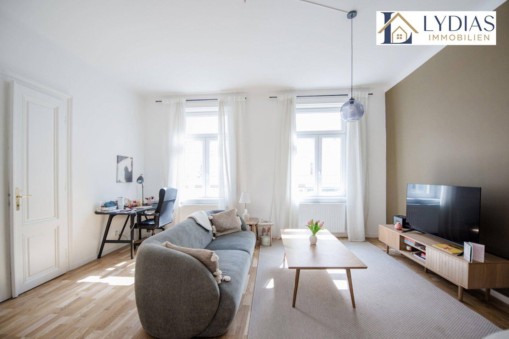 Geräumiges Wohnzimmer mit Holzboden, modernem Sofa und viel Tageslicht.