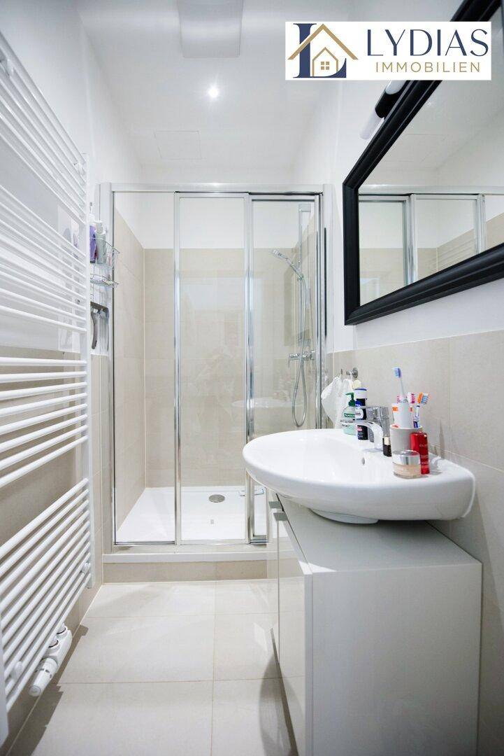 Modernes Badezimmer mit Duschkabine, Waschbecken und beheiztem Handtuchhalter.