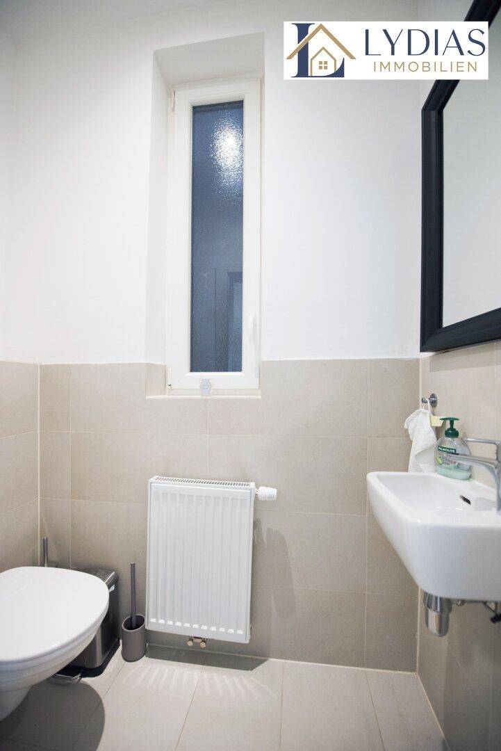 Separates WC mit Waschbecken, Fenster und hellen Fliesen.