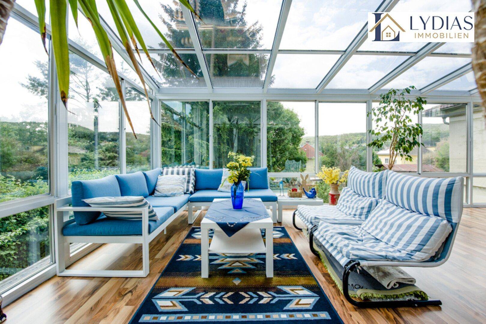 Gemütlicher Wintergarten mit blauen Sofas, Holzboden und weitem Blick ins Grüne.