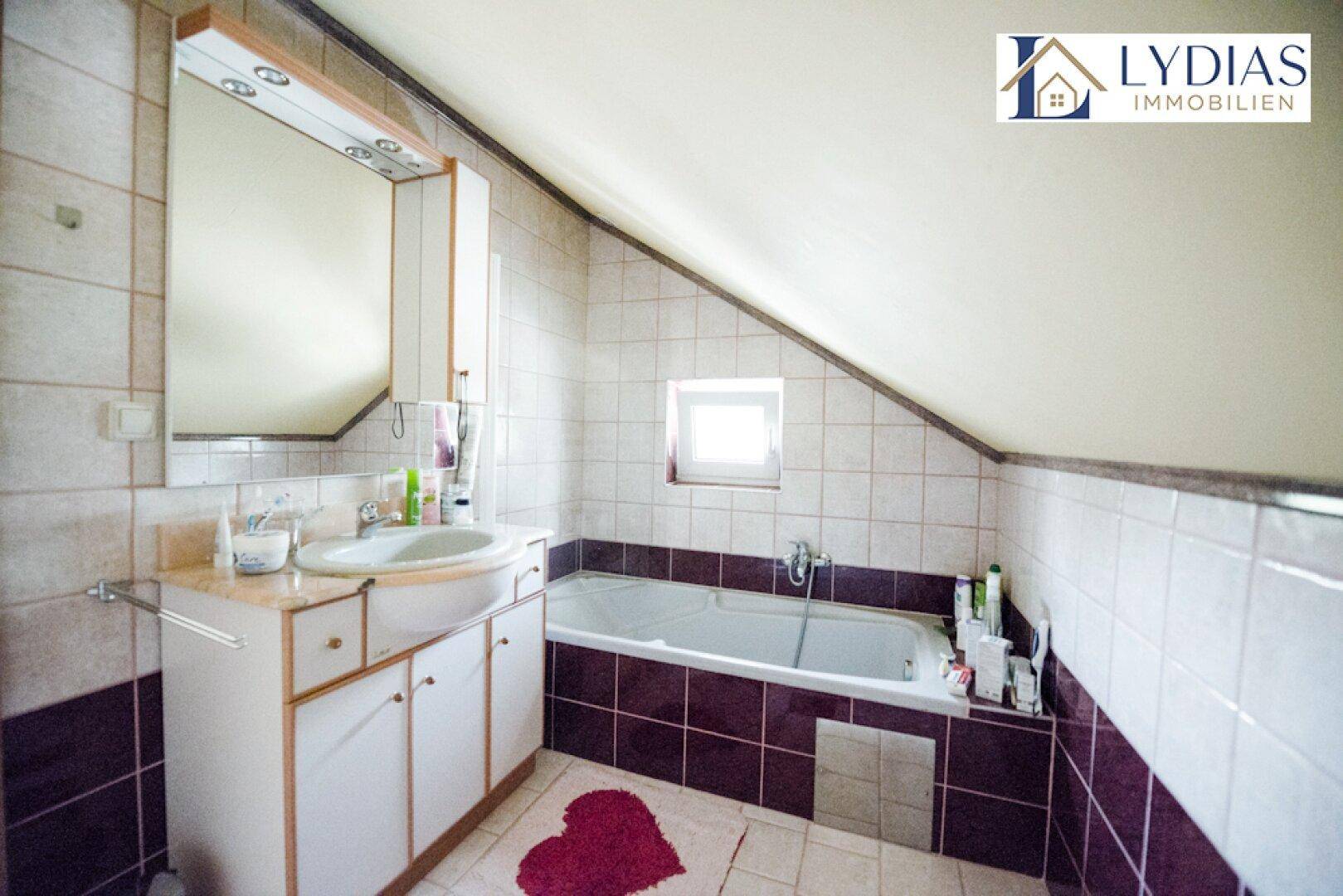 Badezimmer im Dachgeschoss mit Badewanne, Waschbecken und Fliesen in zwei Farben.