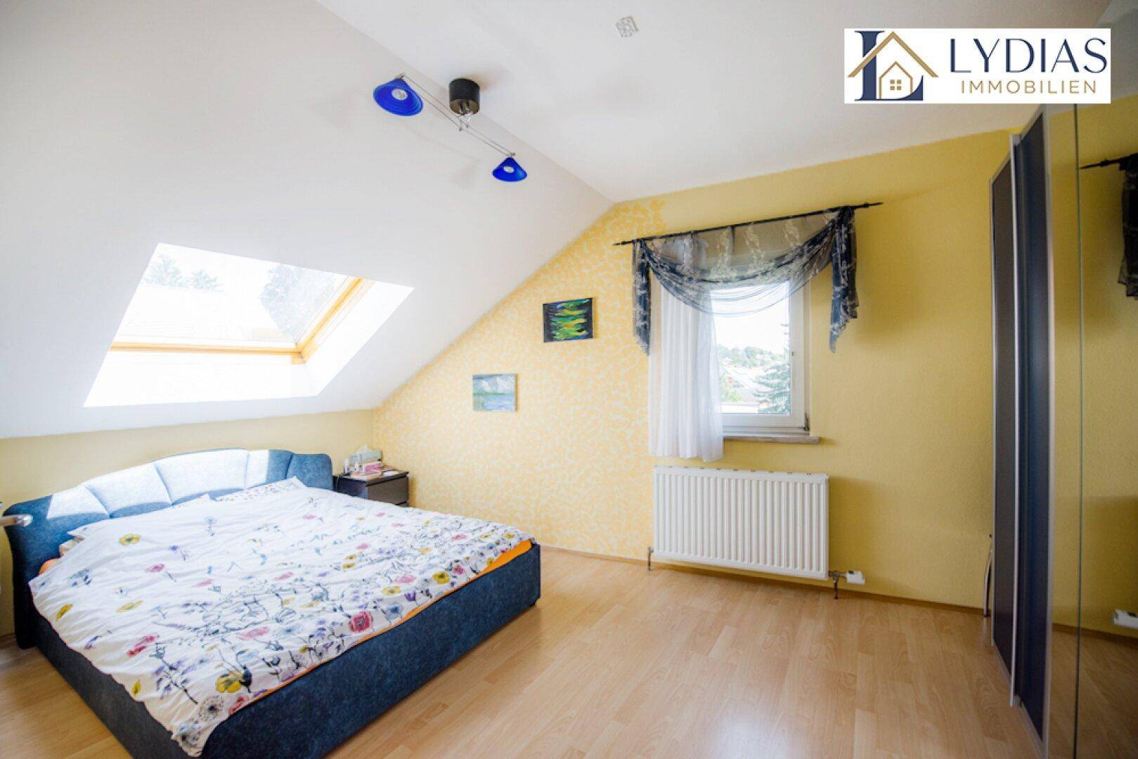 Schlafzimmer im Dachgeschoss mit Dachfenster, gelben Wänden und Laminatboden.