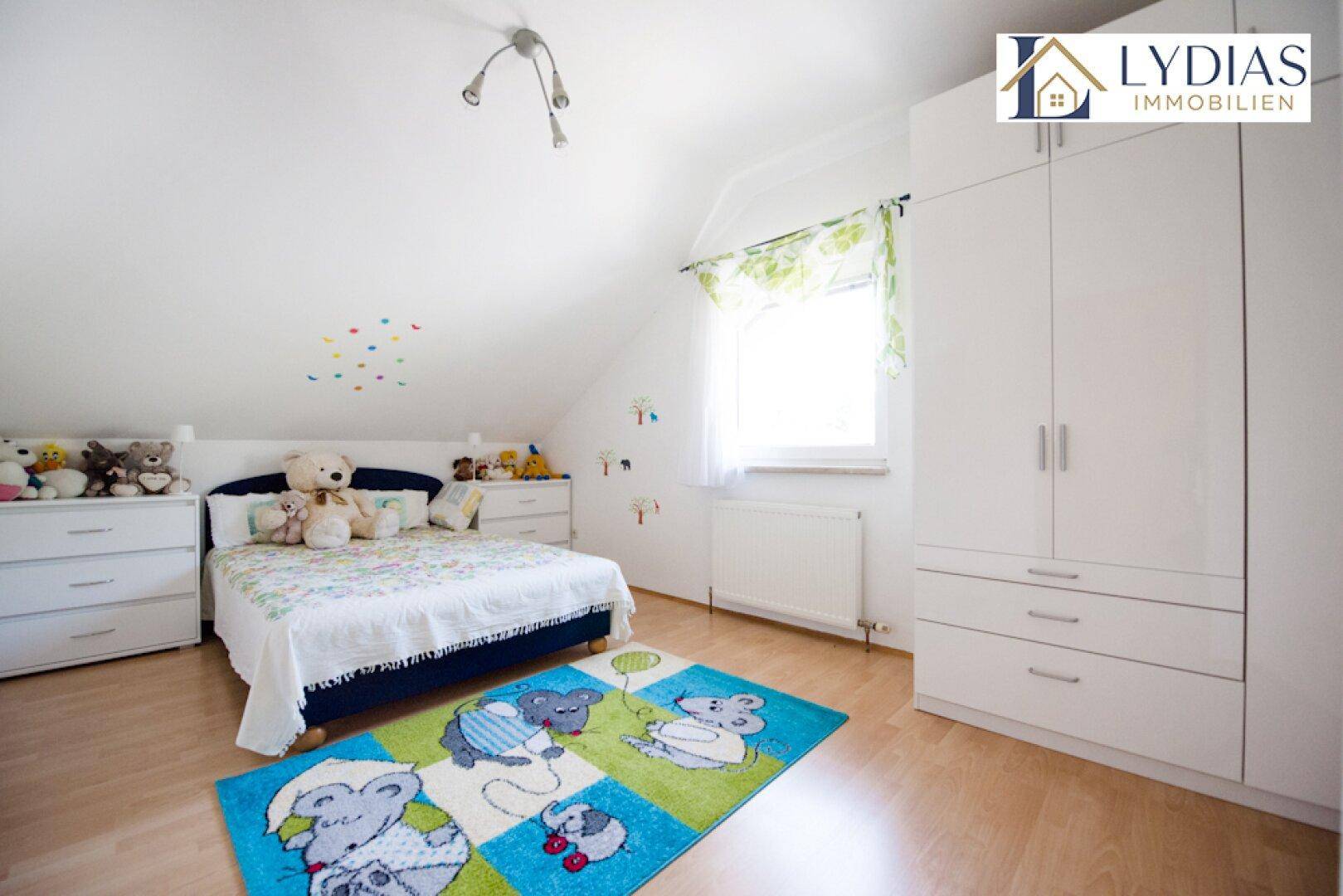Kinderzimmer im Dachgeschoss mit Laminatboden, weißem Kleiderschrank und Spielteppich.