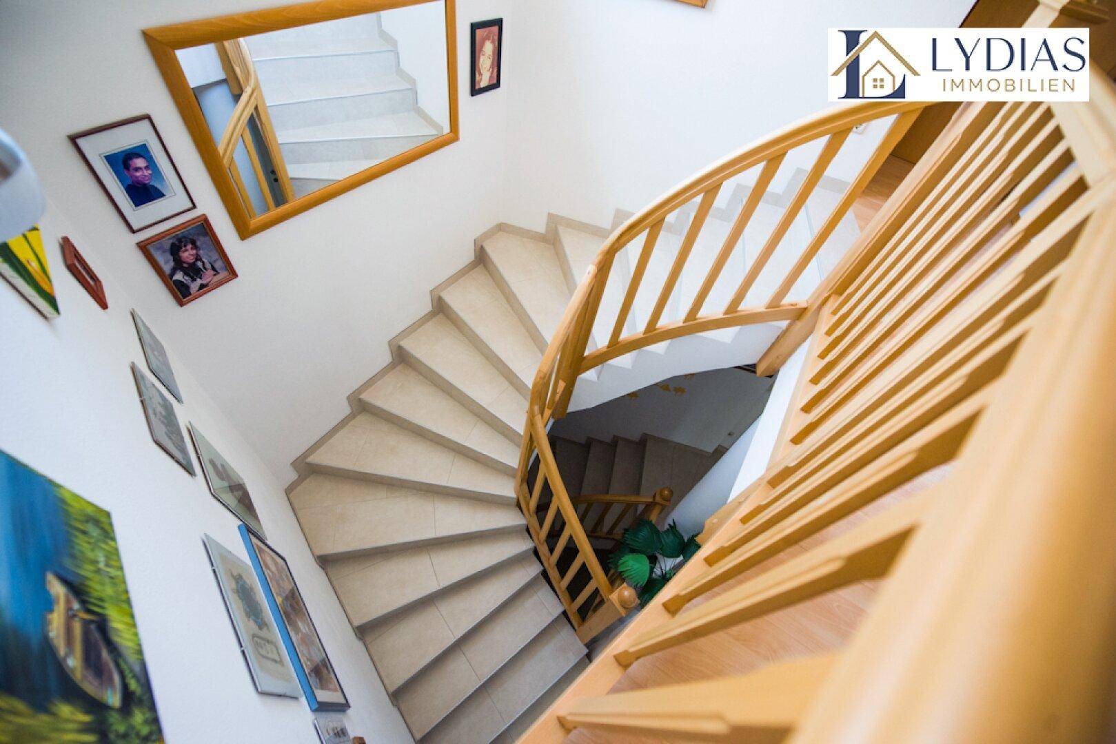 Geschwungene Holztreppe mit hellem Geländer und Bildern an der Wand.