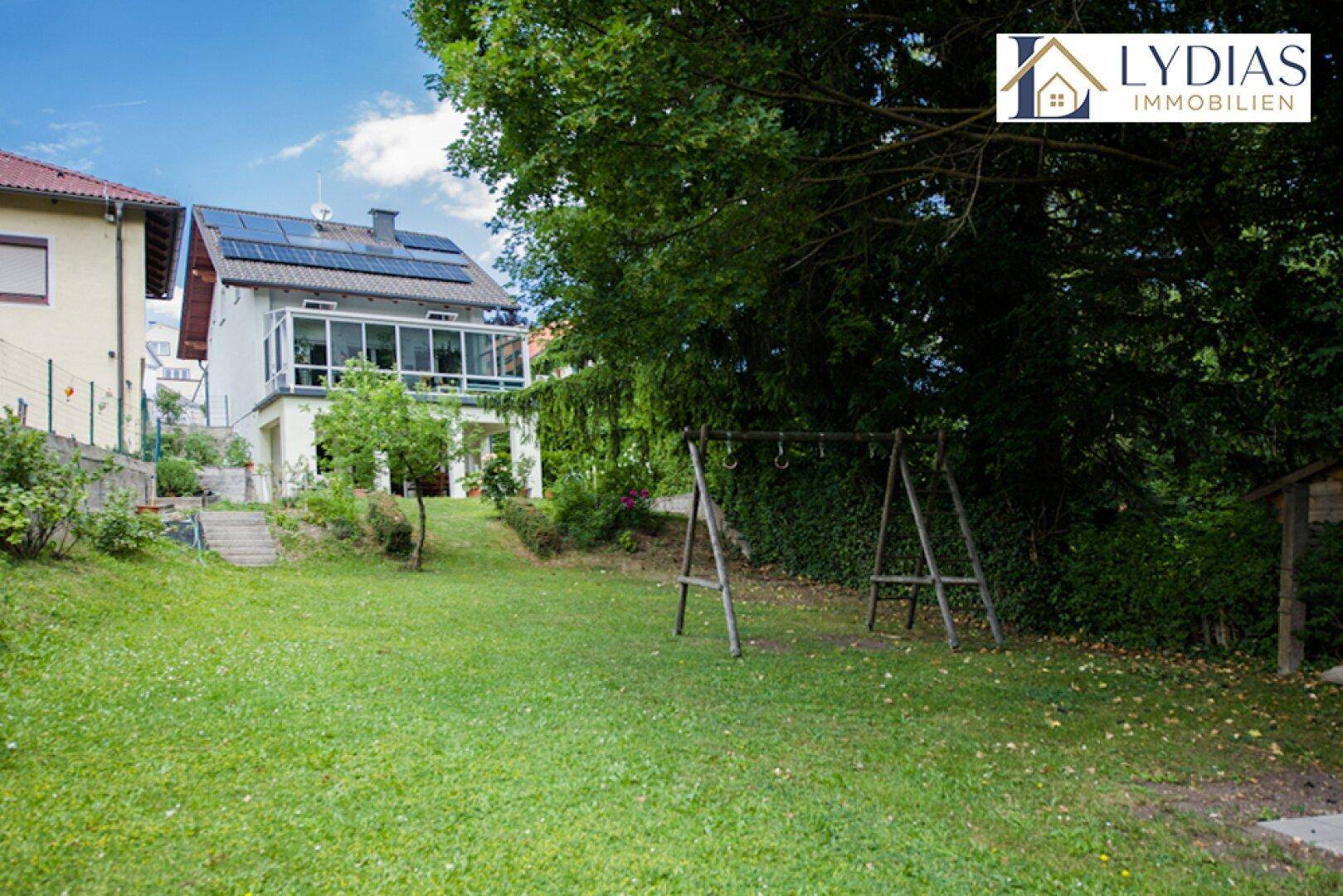 Großer Garten mit Rasenfläche, Bäumen und einem Schaukelgerüst für Kinder.