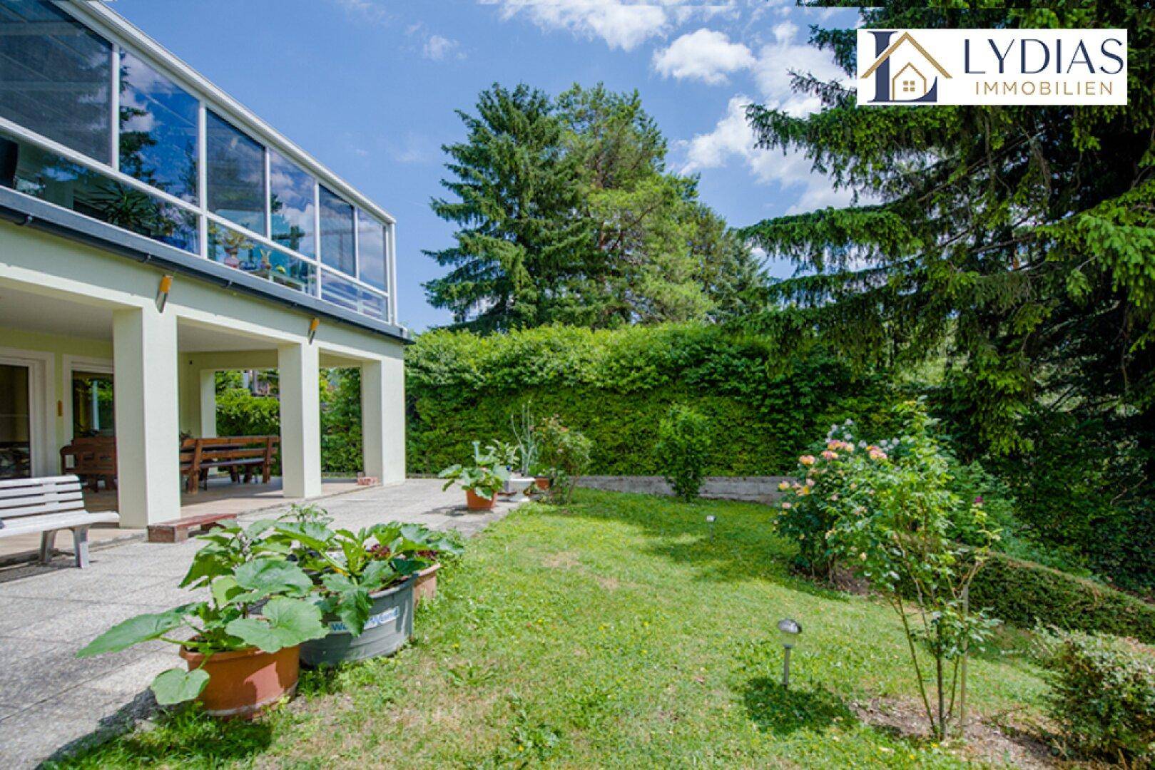 Gepflegter Garten mit Rasen, Bäumen und einer Terrasse am Haus.