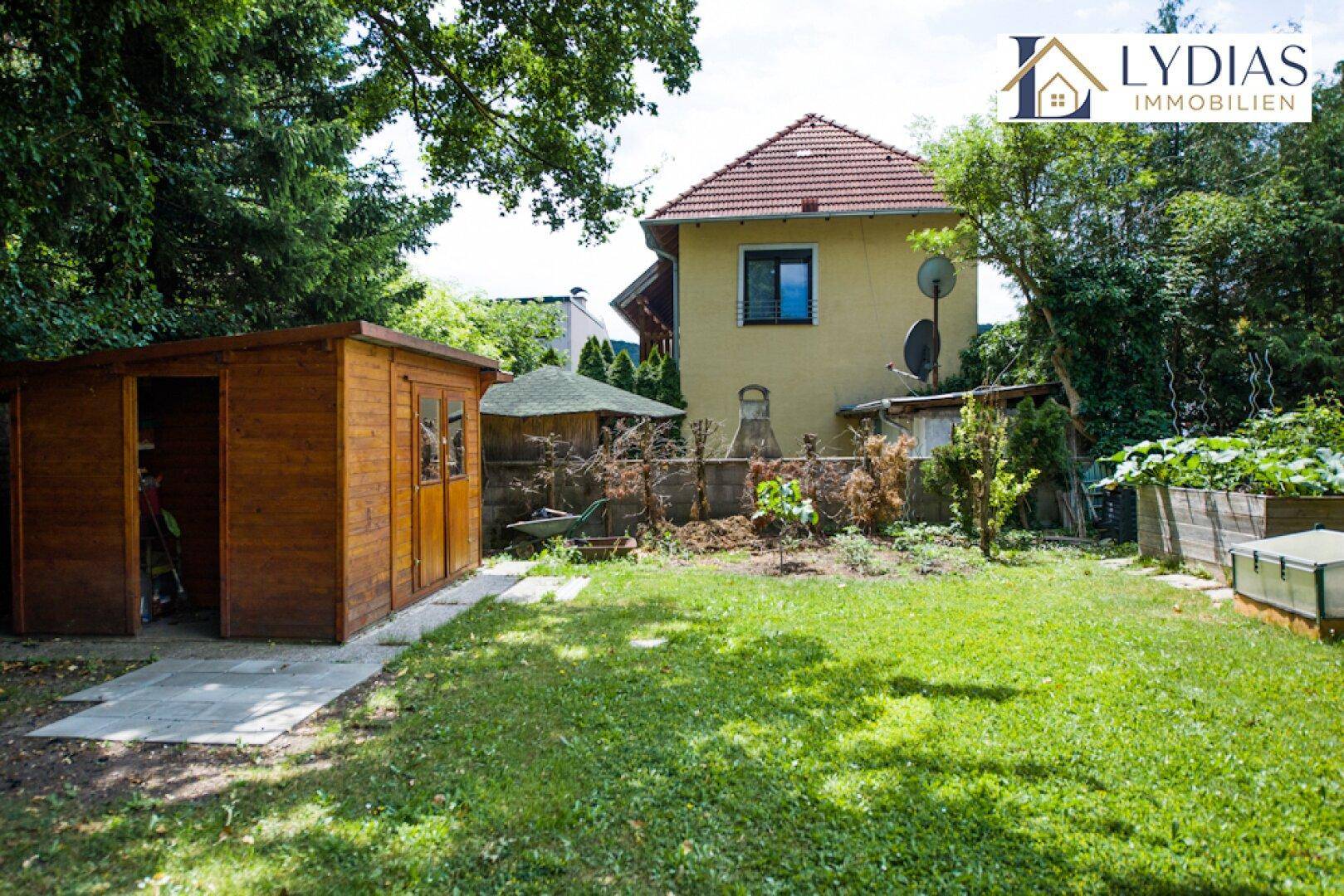 Gartenbereich mit Holzschuppen, Hochbeeten und viel Grünfläche.