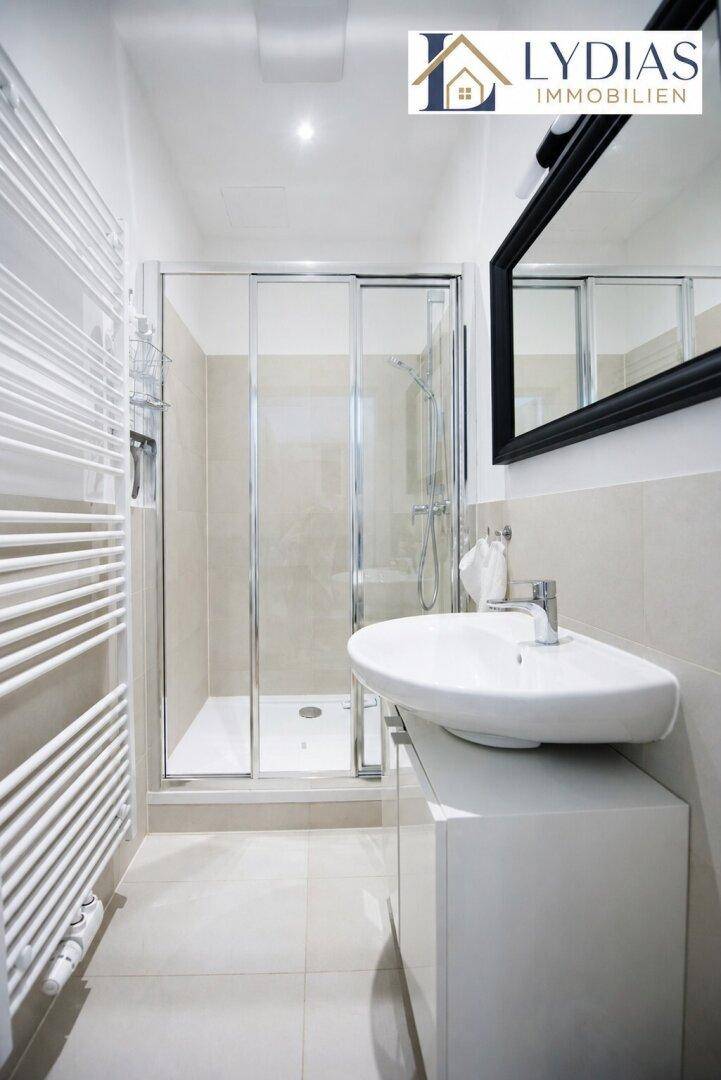 Modernes Badezimmer mit Duschkabine, Waschbecken und beheiztem Handtuchhalter.