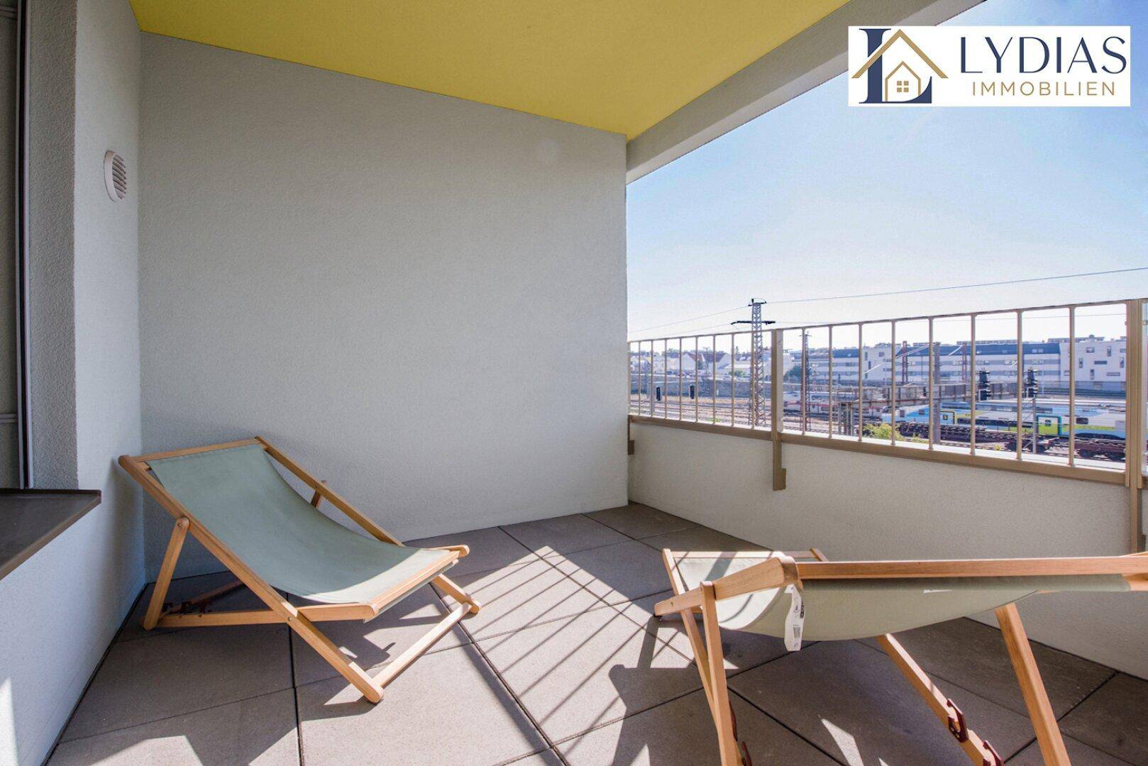 Leerer Balkon mit Fliesenboden und Blick auf die Bahngleise und die Stadt.