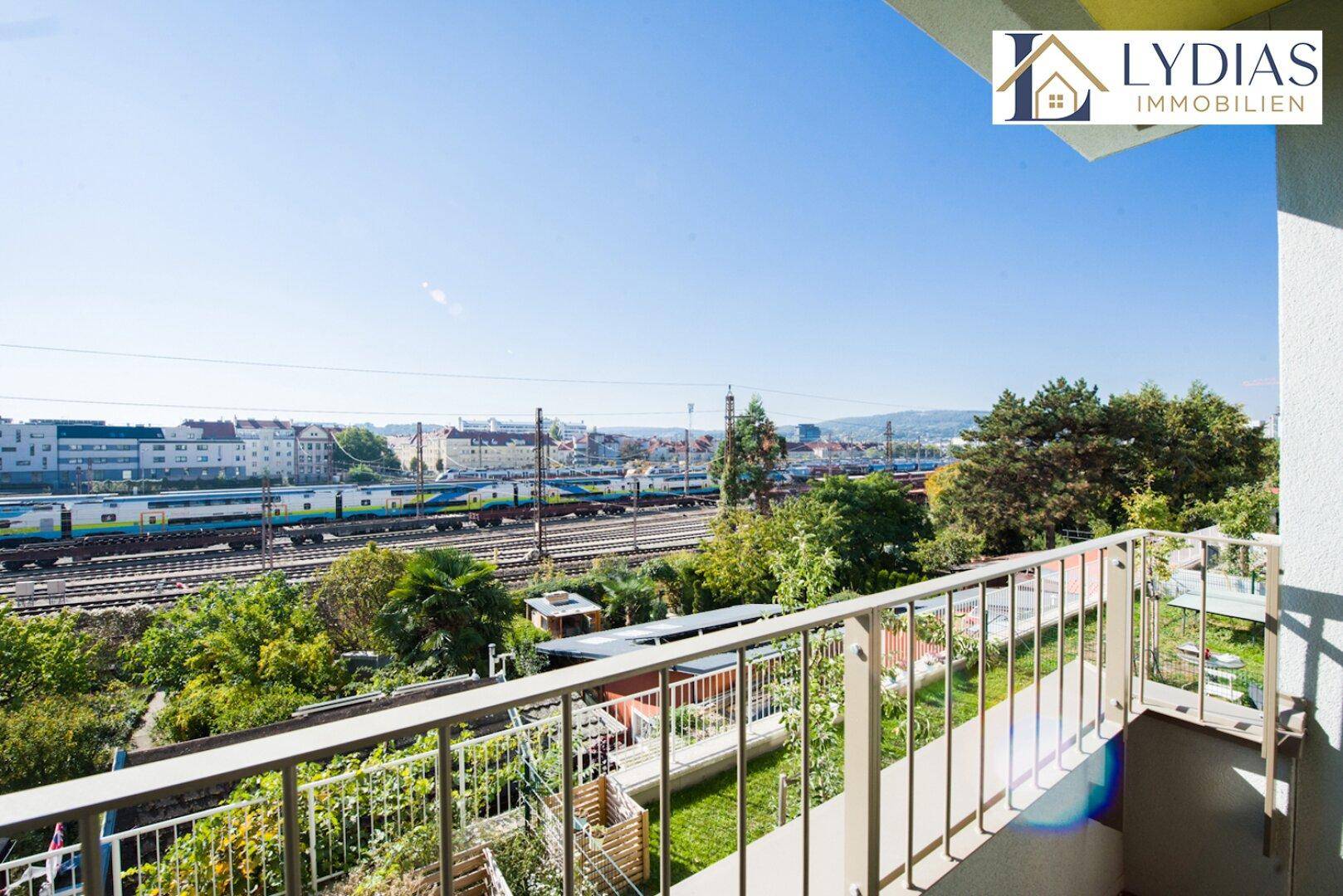 Balkon mit weitem Blick über die Bahngleise, grüne Bäume und die städtische Umgebung.